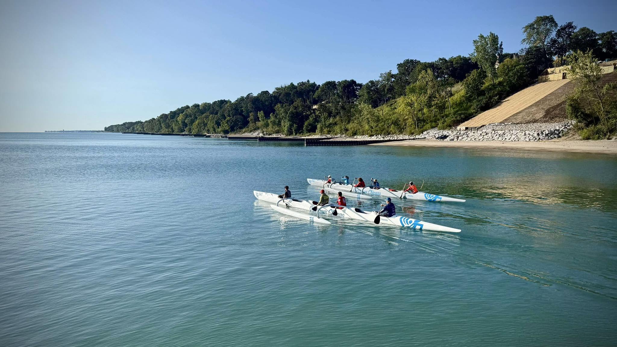 Two Outrigger Chicago OC6 crews paddling on Lake Michigan along the North Shore Yacht Club shoreline